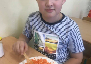 Uczeń miesza pokrojoną marchewkę na talerzu